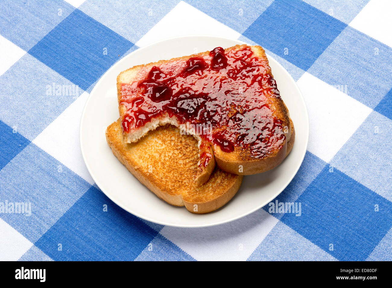 Freschi, pane tostato caldo spalmata con gelatina di uva si siede con un morso preso fuori di esso durante il pasto. Foto Stock