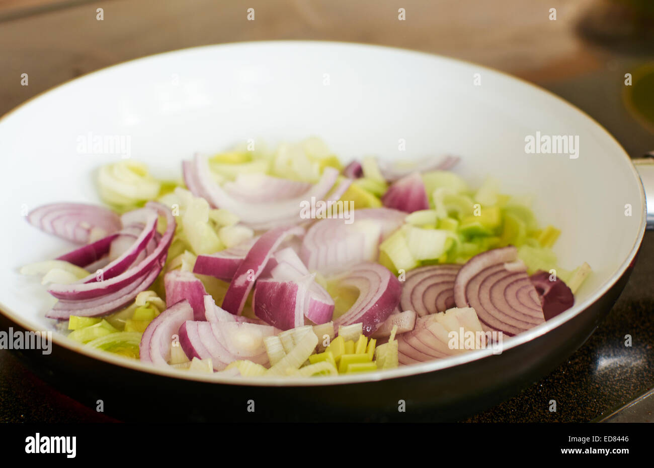 Cipolla rossa e il porro essendo soffritto in una coppa in ceramica. Foto Stock