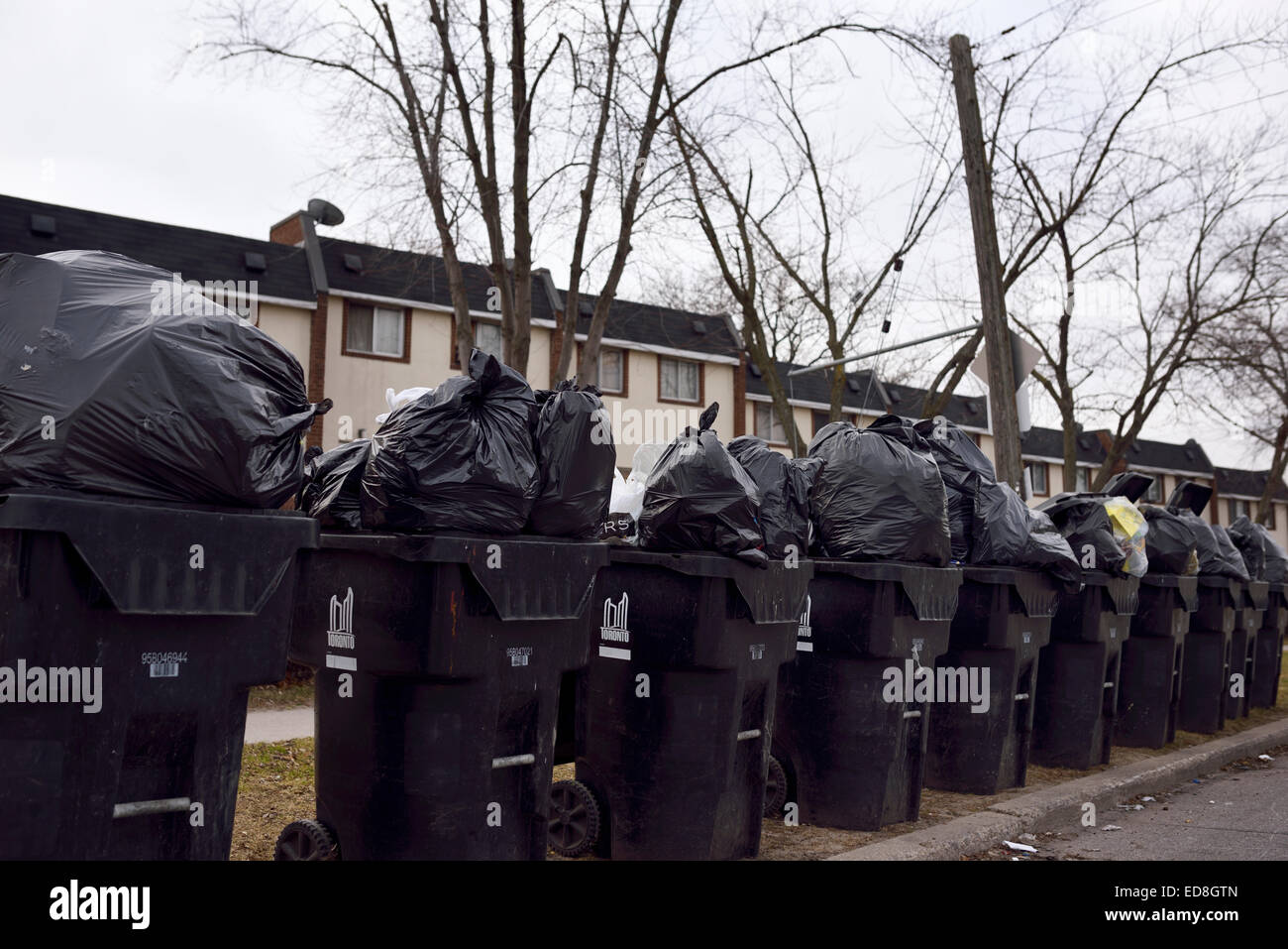 Traboccante di garbage impilati in fila di contenitori su strada in attesa di ritiro Foto Stock