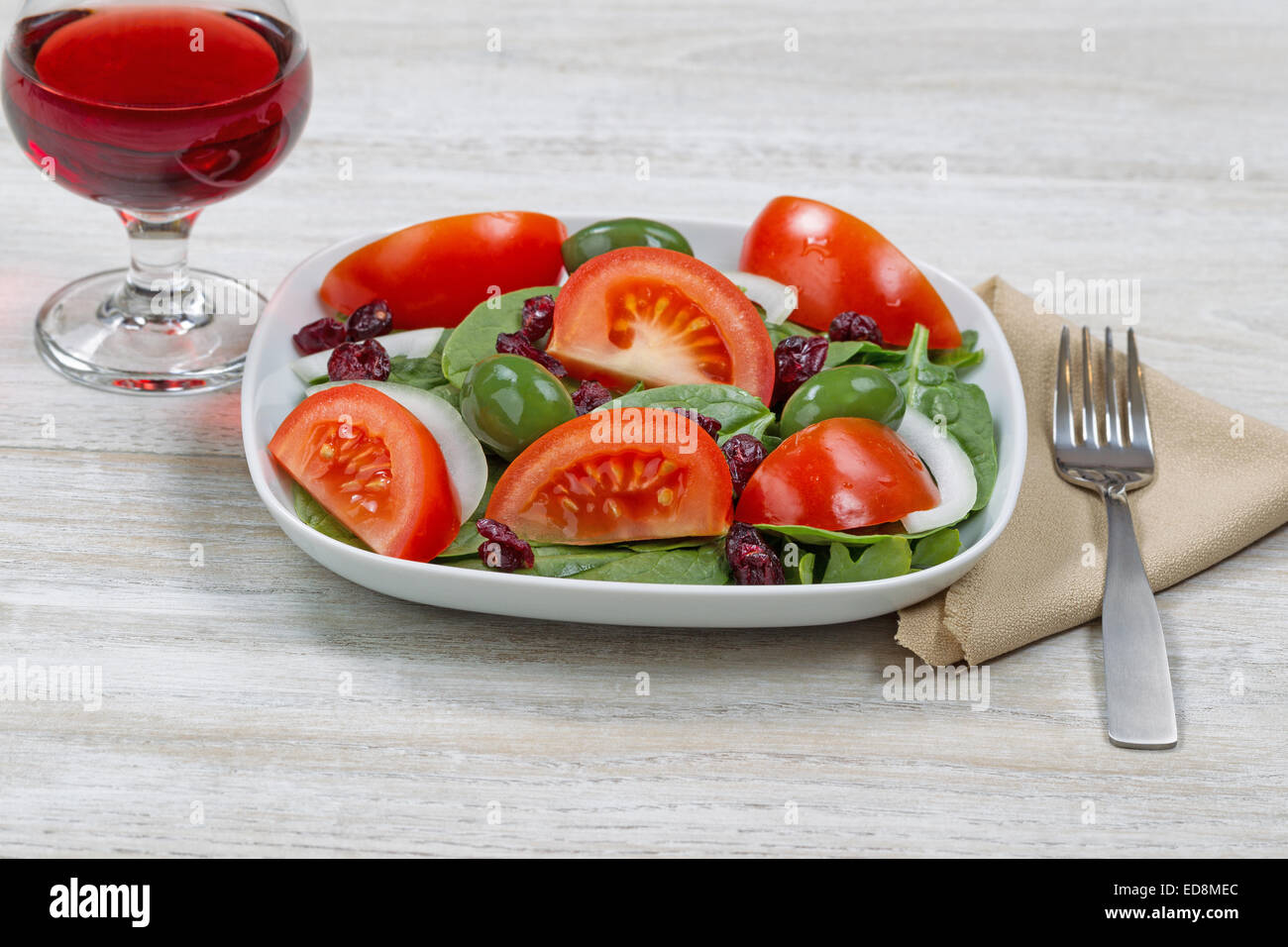 Vista frontale immagine di un fresco insalata di spinaci in piastra bianca con un bicchiere di vino rosso e la forcella con un panno assorbente su bianco woo Foto Stock