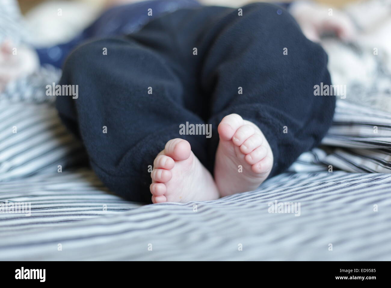 Piedi del bambino su un letto con lenzuola a strisce Foto Stock