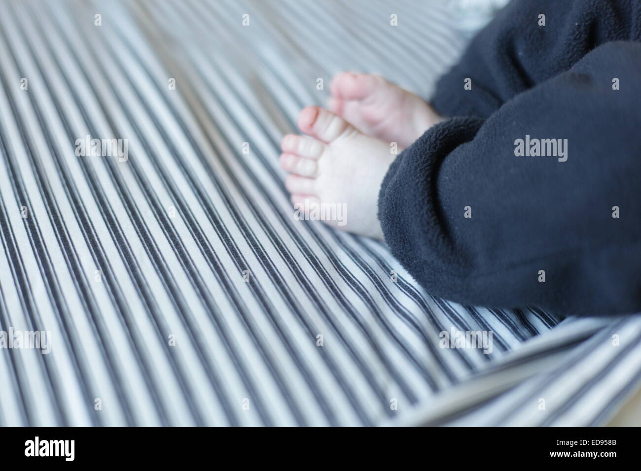 Piedi del bambino su un letto con lenzuola a strisce Foto Stock