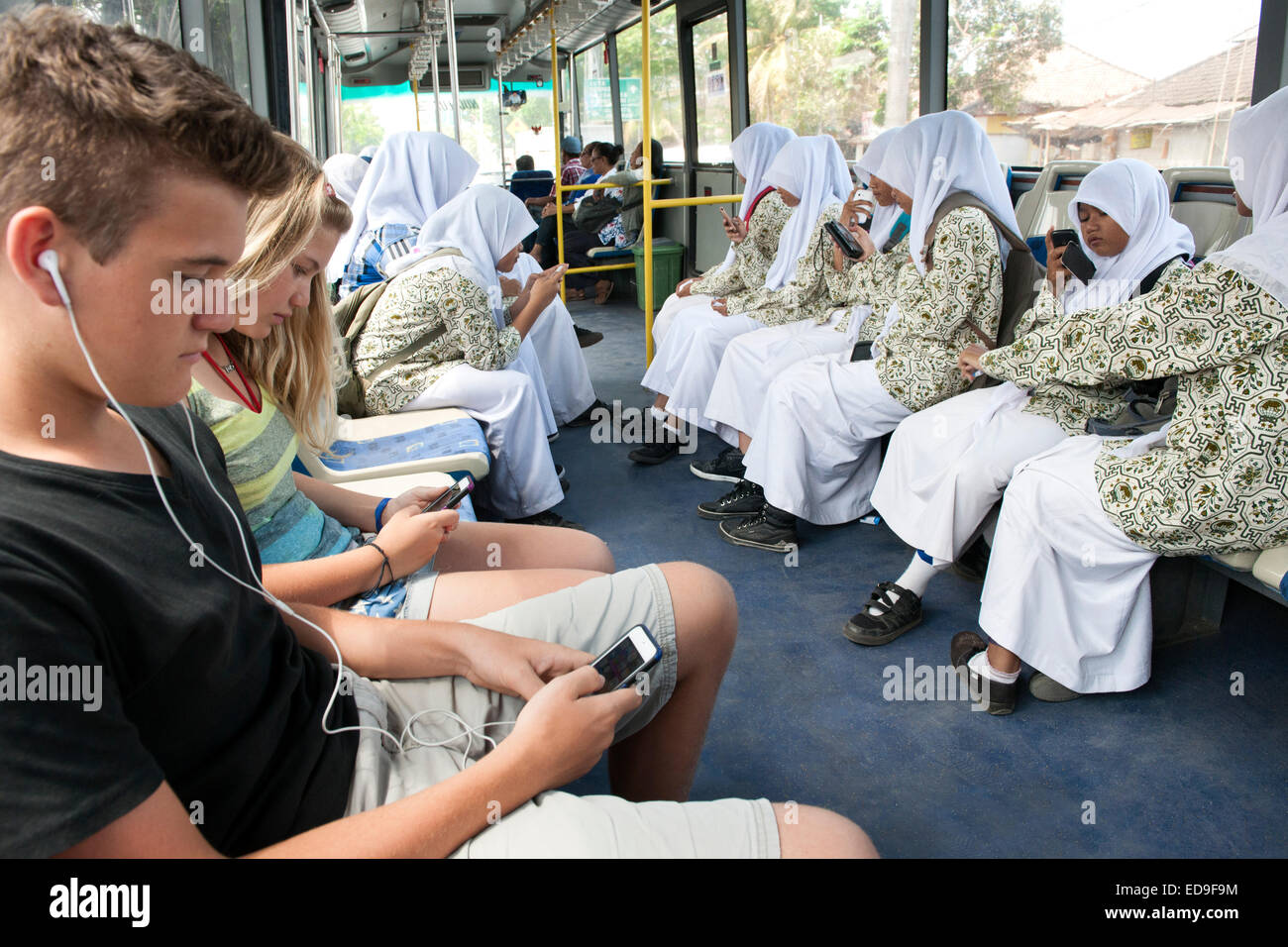 Scuola Balinese ragazze e due bambini occidentali con i loro telefoni smart e ipod su un bus di Bali, Indonesia. Foto Stock