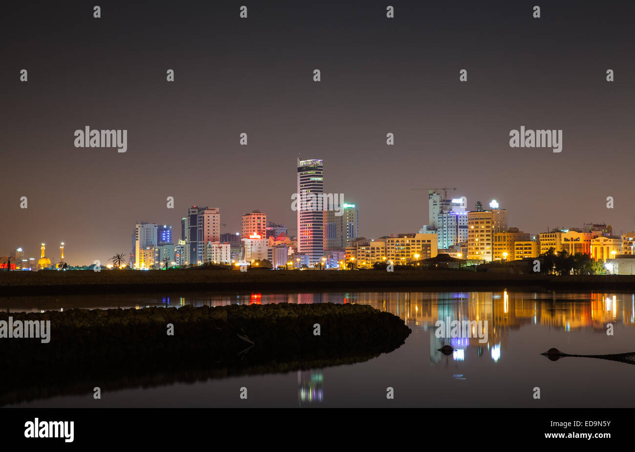 La notte dello skyline della città splendente luci al neon e riflessi nell'acqua. Manama, Bahrein, Medio Oriente Foto Stock