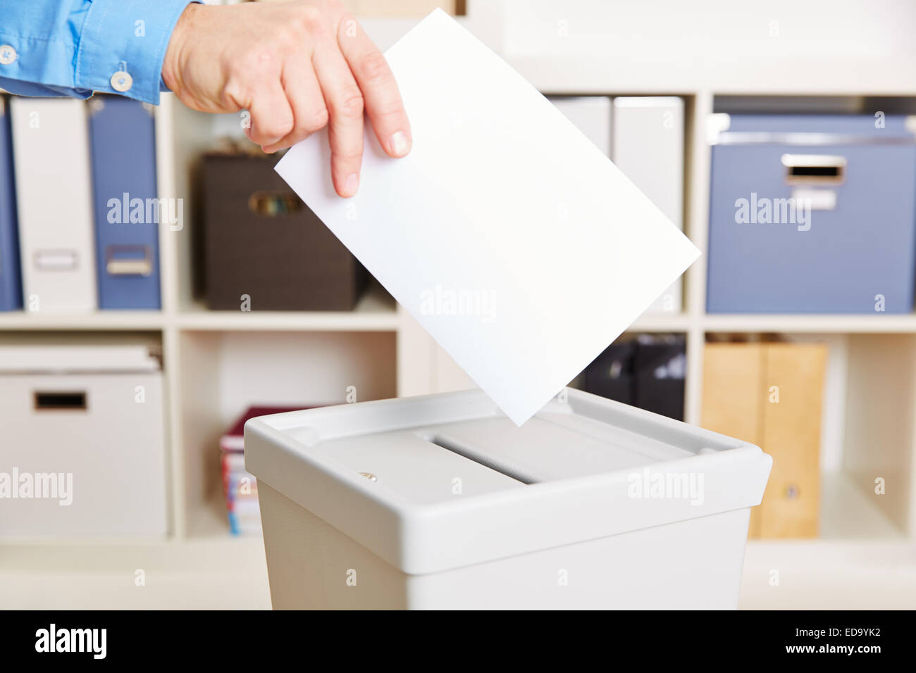 Mano con voto cartaceo e cabina elettorale nella stazione di polling Foto Stock