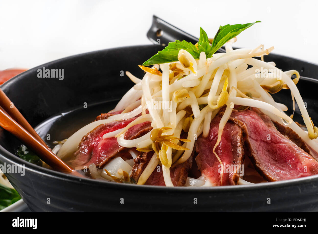 Pho - Vietnamita raro manzo zuppe su sfondo bianco con salsa hoisin, salsa piccante, spezie, beansprouts, e basilico fresco Foto Stock