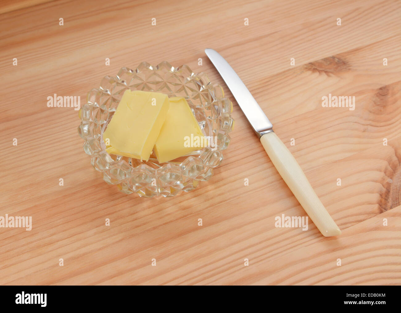 Il burro in un piatto di vetro con un piccolo coltello per spalmatura su una pineta tabella Foto Stock