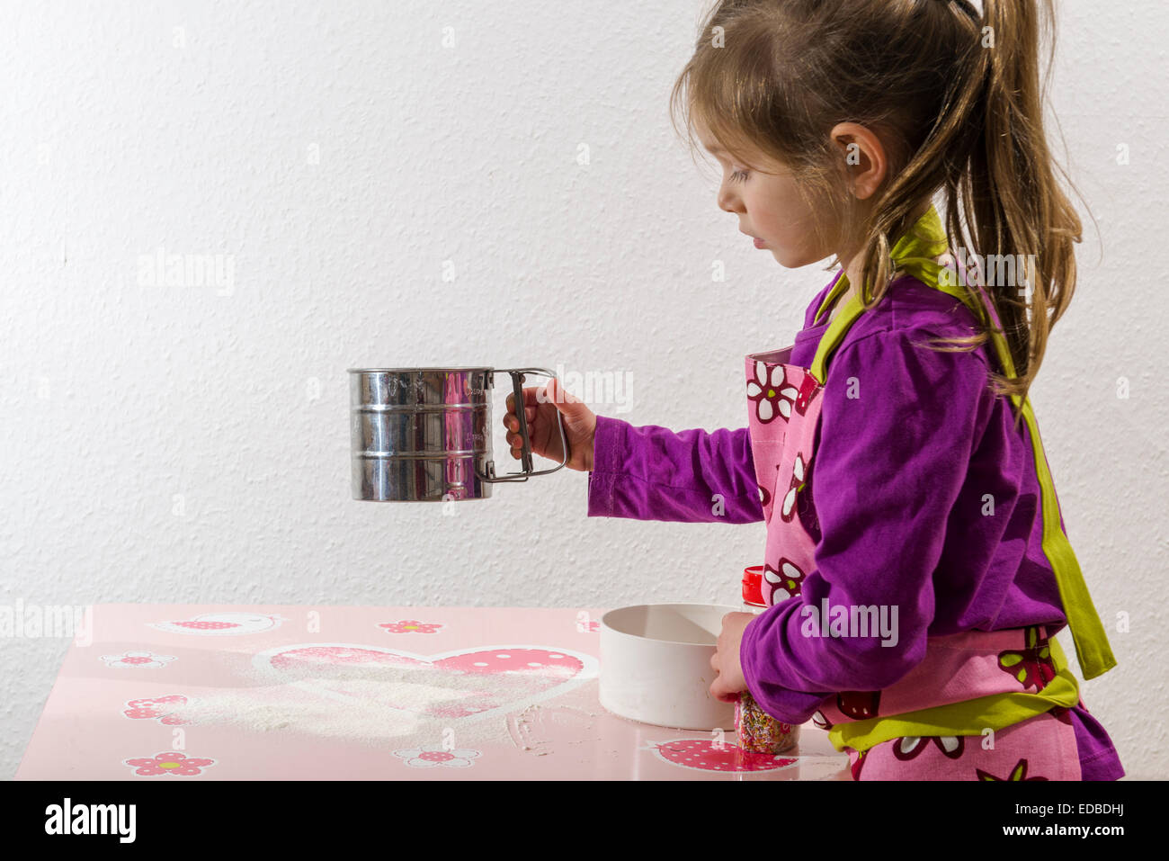 Ragazza 3 anni, cottura, spolverata di farina su un tavolo Foto Stock