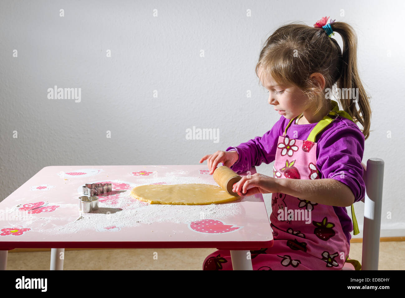 Ragazza 3 anni, cottura biscotti di Natale, stendere la pasta su un tavolo Foto Stock
