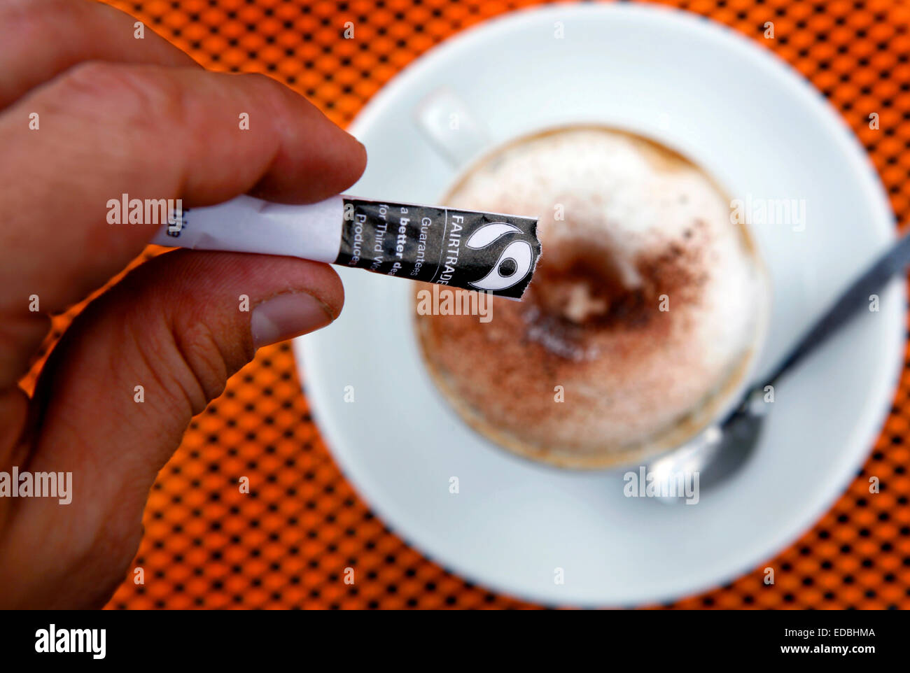 Un uomo versando Fairtrade zucchero nel suo cappuccino a Londra Foto Stock