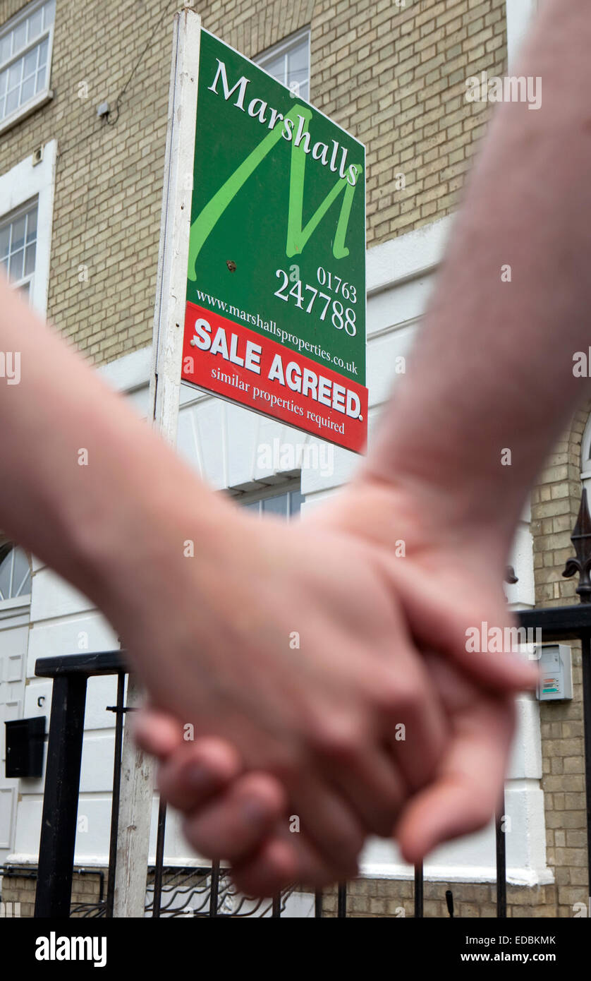 Una giovane coppia sperando di poter immettere sul mercato immobiliare sono mostrati attorno a una casa da un agente immobiliare Foto Stock