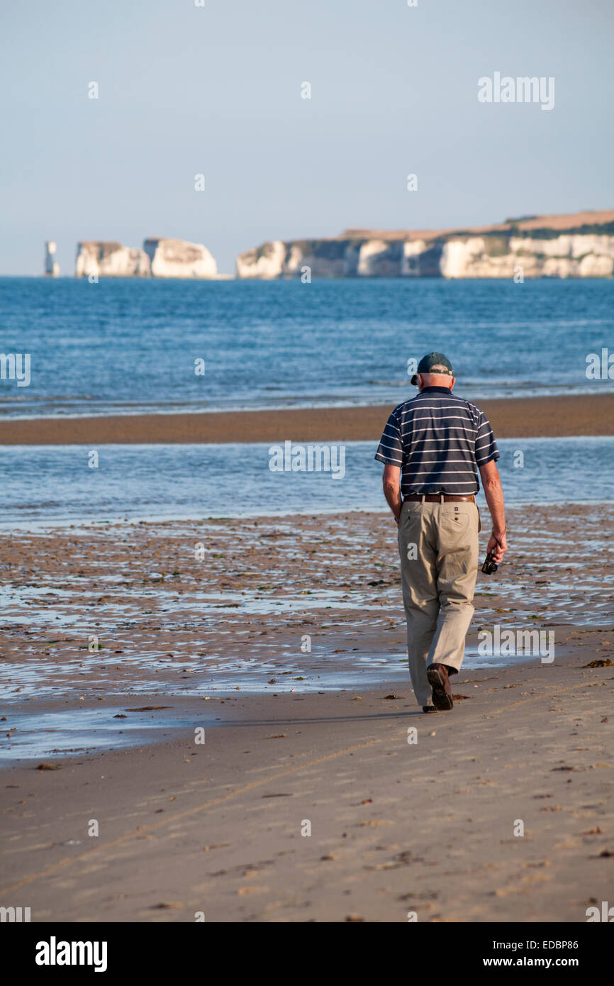 Man tenere la fotocamera a piedi lungo la spiaggia di Studland con il vecchio Harry rocce al di fuori della messa a fuoco a distanza su una sera di luglio Foto Stock