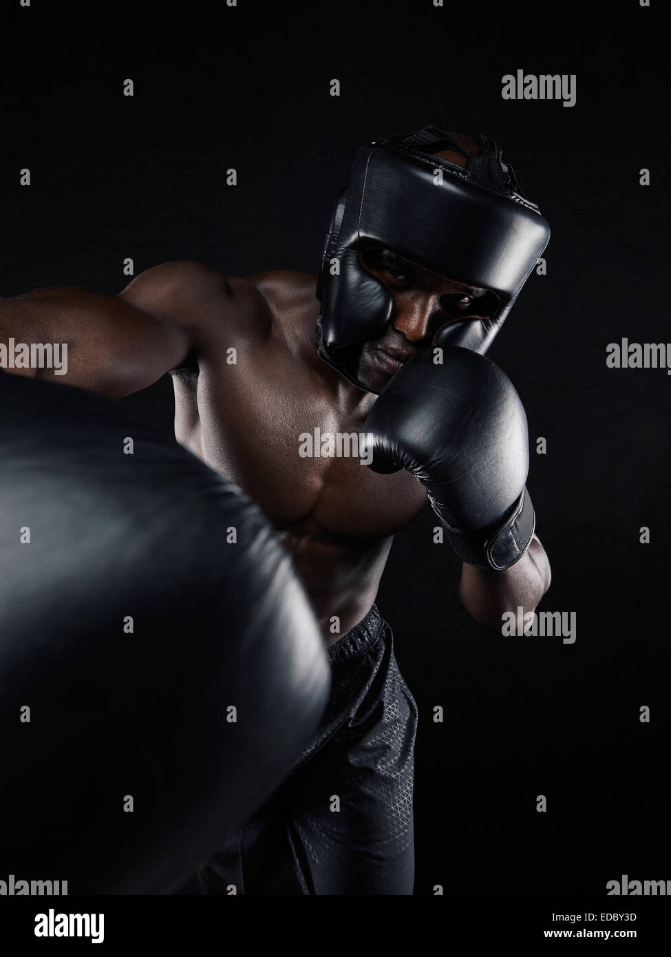 Ritratto di un giovane pugile gettando un punzone in telecamera mentre si pratica su sfondo nero. Atleta maschio indossando guanti di inscatolamento Foto Stock