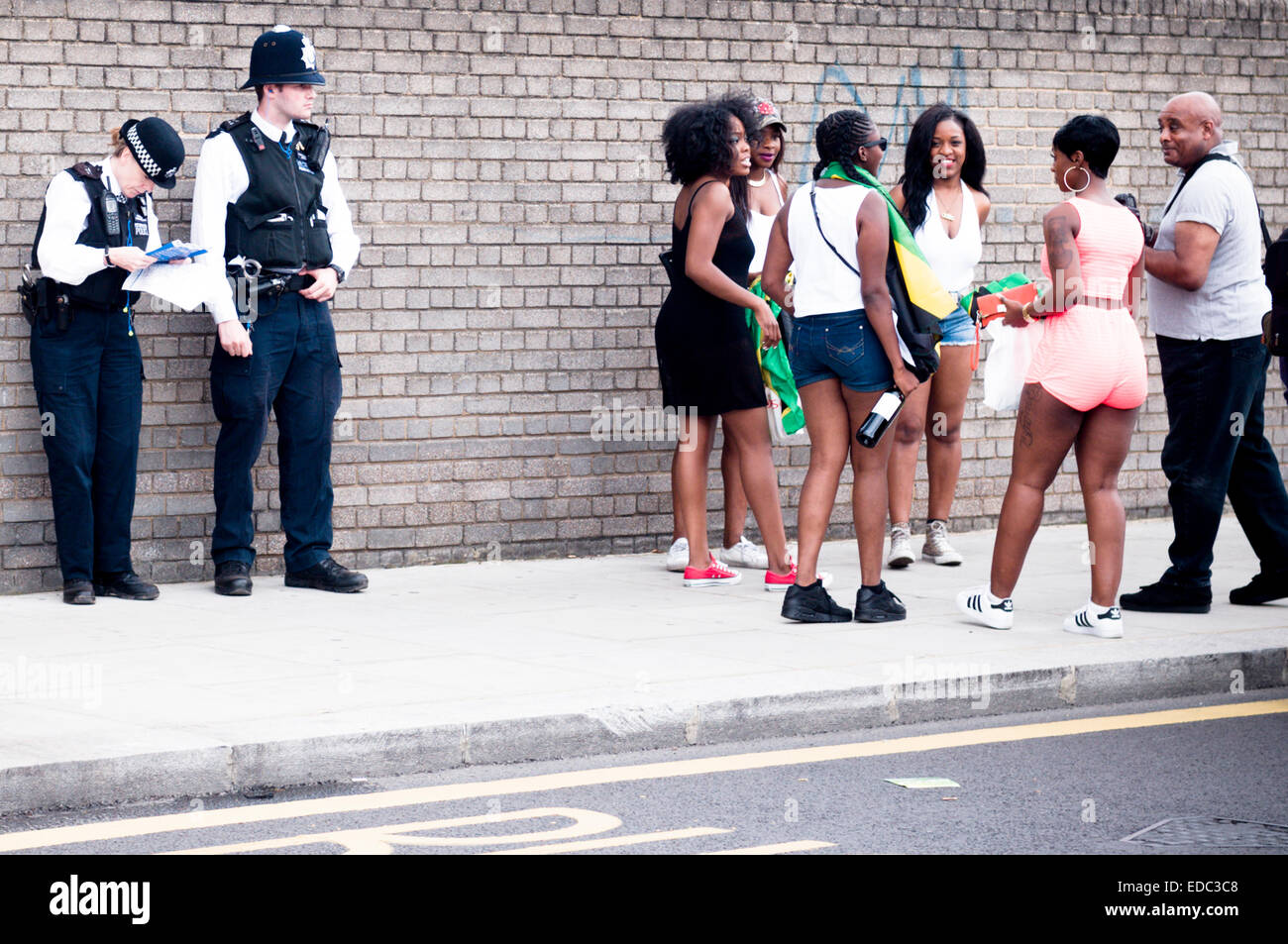 LONDON, Regno Unito - 24 agosto 2014: carnevale di Notting Hill, un gruppo di persone che si riuniscono accanto a due poliziotti in piedi Foto Stock