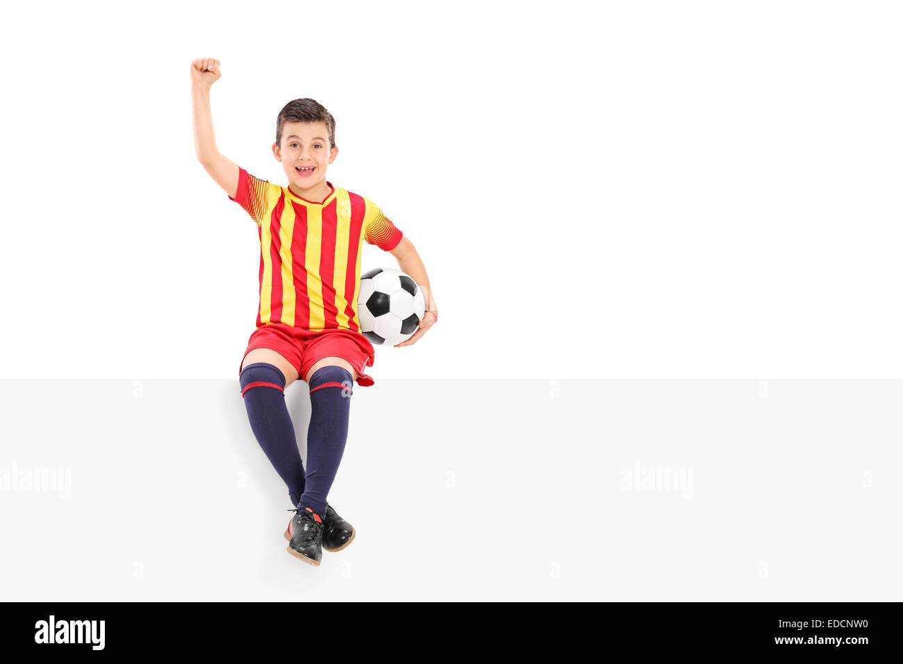 Junior Soccer player gesticolando gioia seduto su un pannello isolato su sfondo bianco Foto Stock