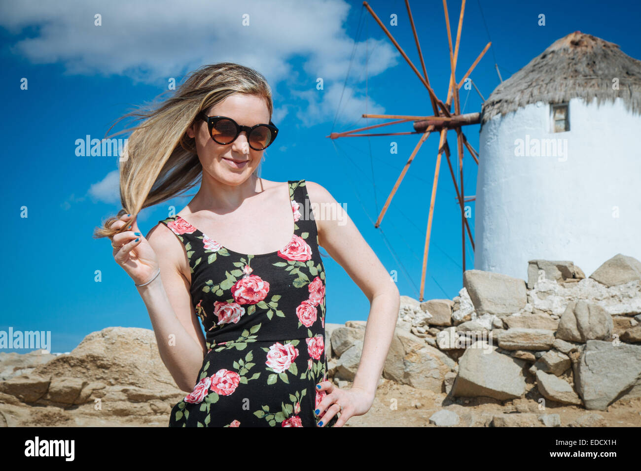 Giovane ragazza bionda con occhiali da sole al mulino a vento a Mykonos Foto Stock