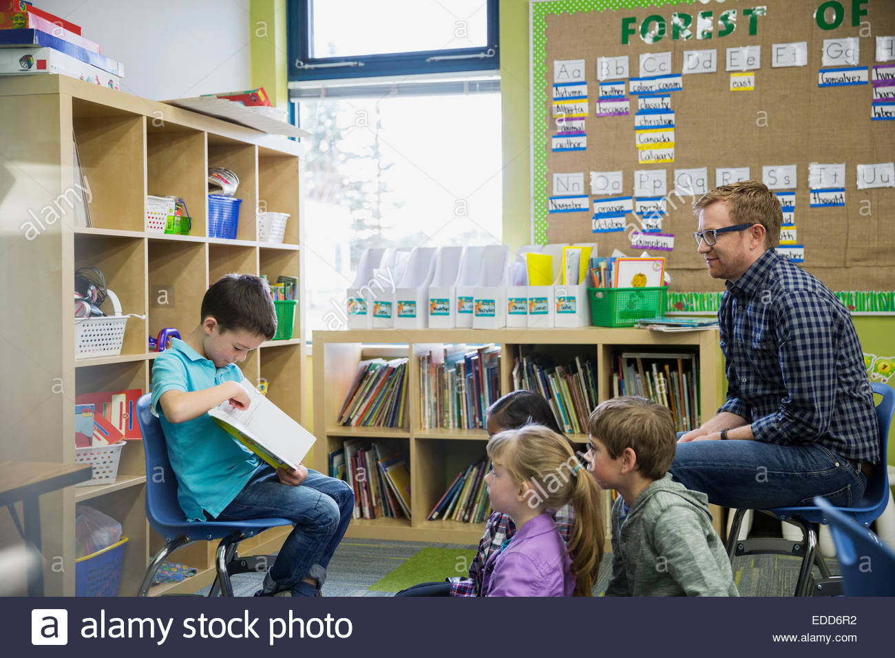 Elementare di lettura degli studenti ai compagni e insegnante Foto Stock