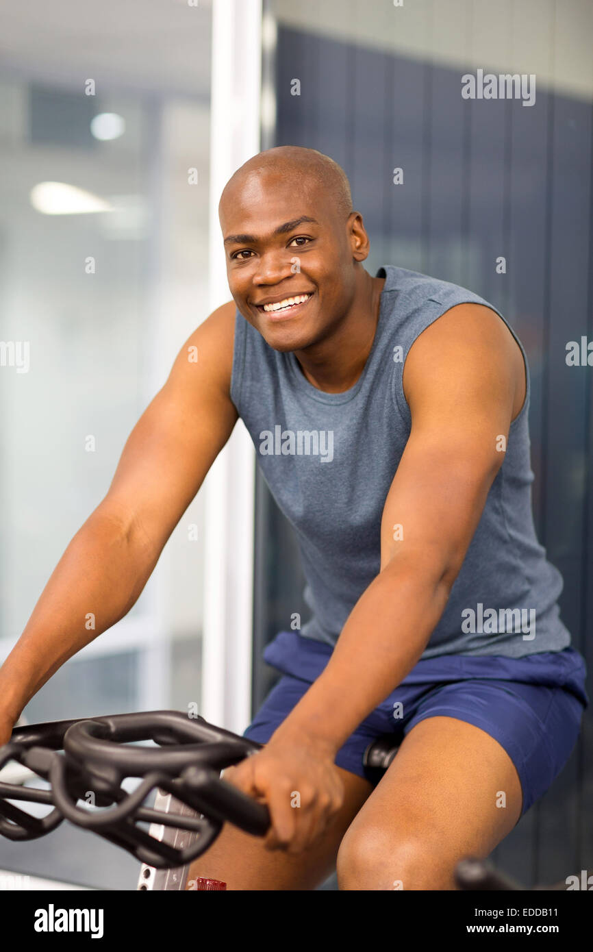 African American seduto su una bicicletta stazionaria in palestra Foto Stock