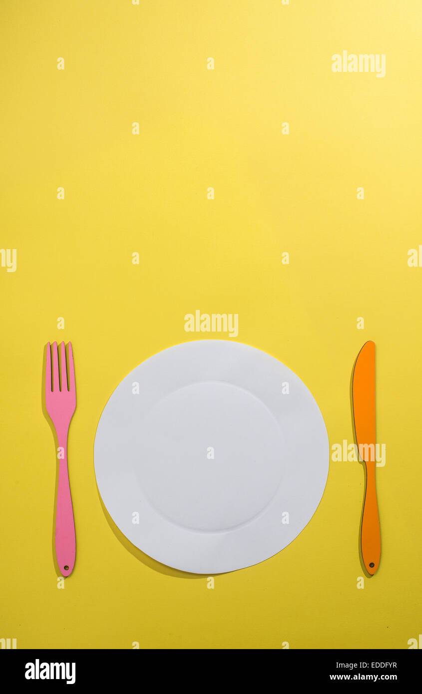 Concetto di alimentare con carta, piastra, forchetta e coltello su sfondo giallo Foto Stock
