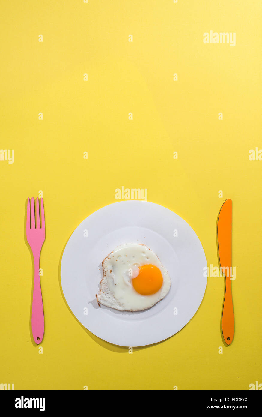 Concetto di alimentare con carta, uovo fritto su piastra, forchetta e coltello su sfondo giallo Foto Stock