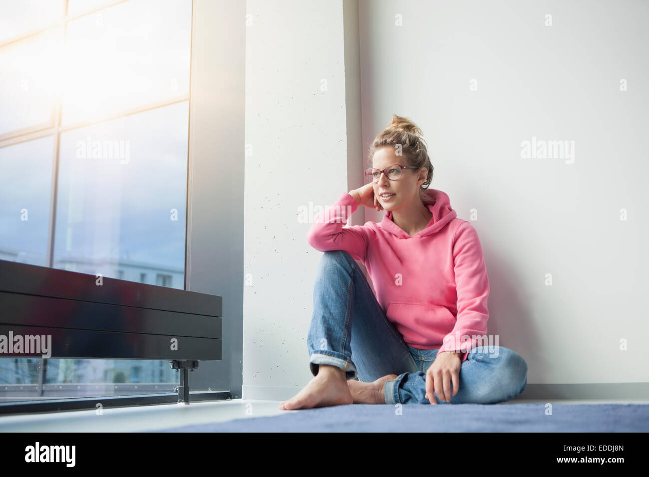 Donna matura seduta sul pavimento al suo appartamento guardando attraverso la finestra Foto Stock