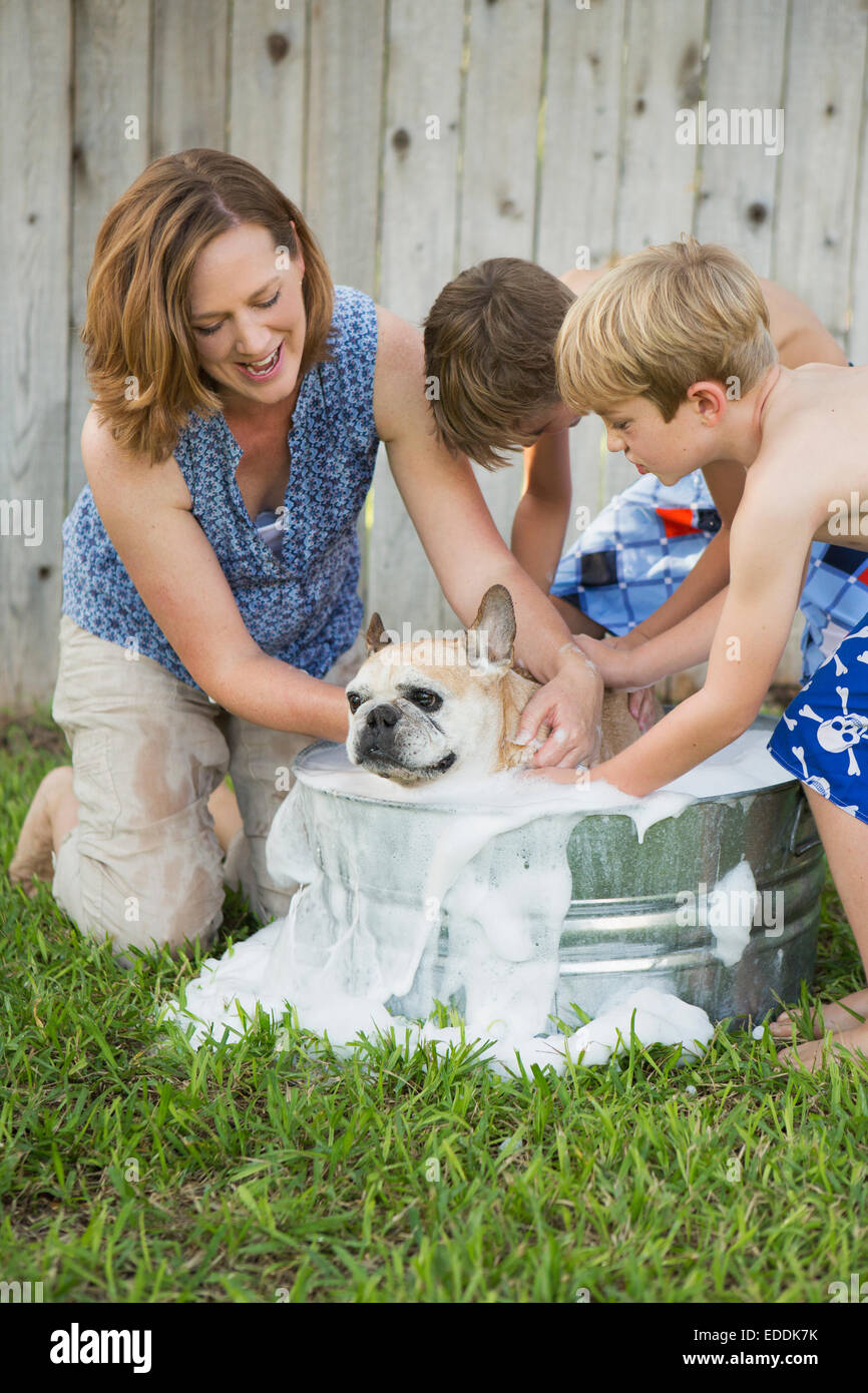 Una famiglia nel loro giardino, il lavaggio di un cane in una vasca. Foto Stock