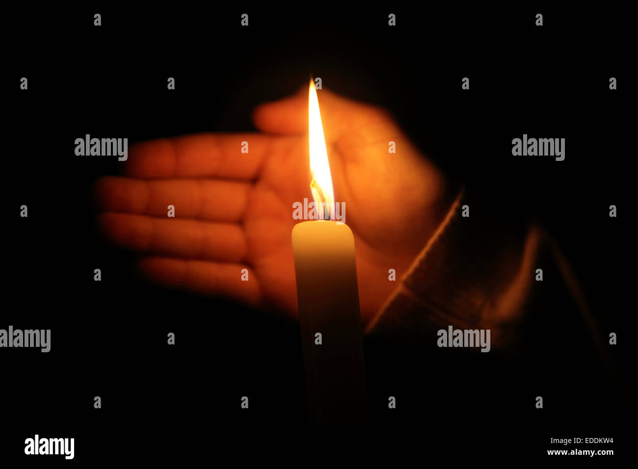 Mano protegge la fiamma di una candela la masterizzazione su uno sfondo scuro Foto Stock