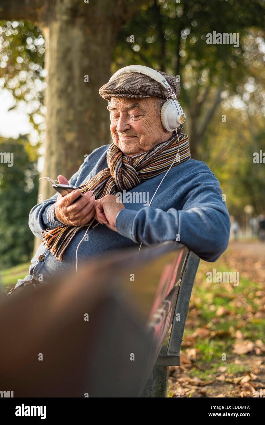 Senior uomo sulla panchina del parco con un telefono cellulare e le cuffie Foto Stock