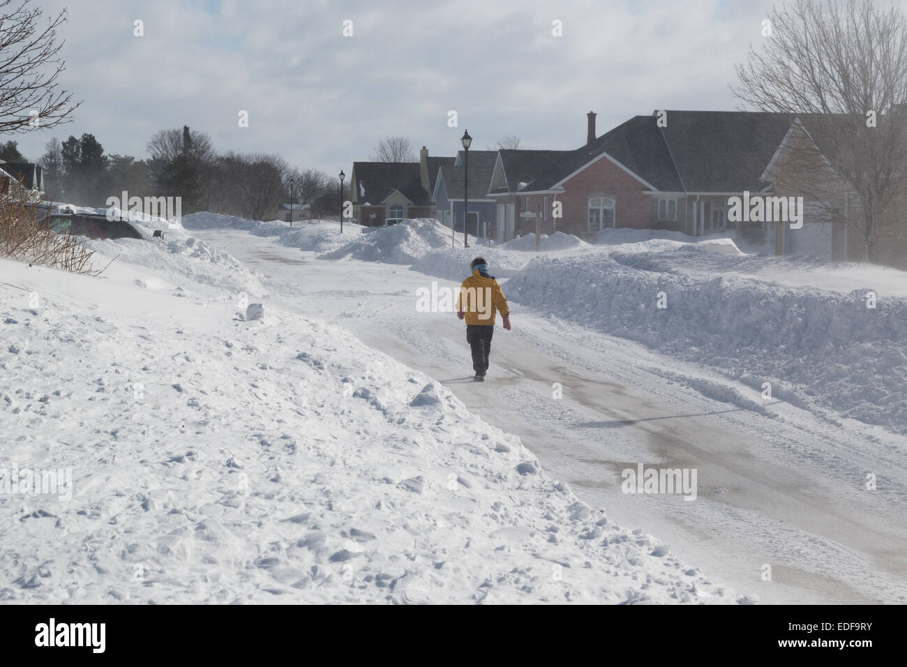 Lone passeggiate pedonali attraverso suburbia mentre il vento fruste la neve selvaggiamente intorno a lei. Foto Stock