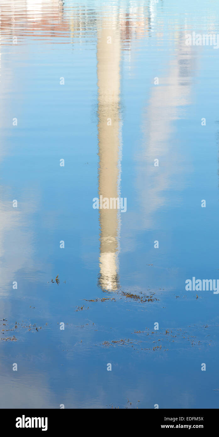 Un fumaiolo invertito in una riflessione di acqua salata con alghe galleggianti e le nuvole nel cielo blu. Foto Stock