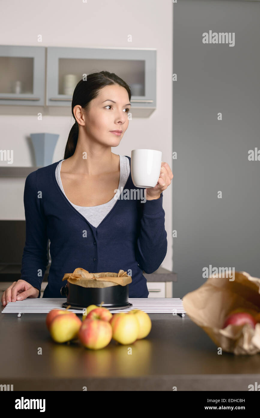 Sorridente giovane donna la cottura crostata di mele in piedi con una teglia da forno appena rimosso dal forno su di un impianto di raffreddamento Foto Stock