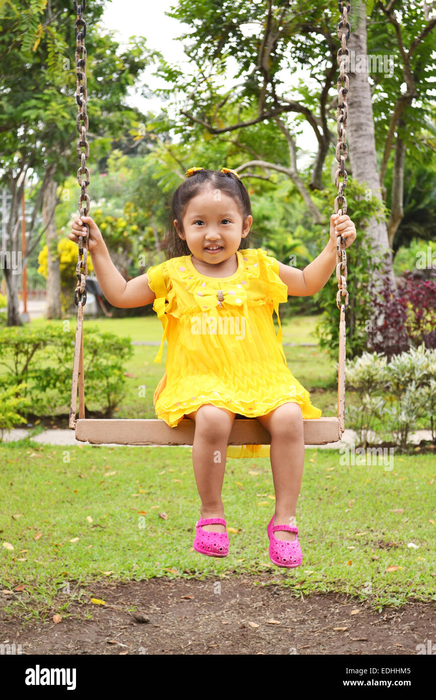 Carino asiatica di bambini che giocano su altalena indossando bello abito giallo Foto Stock