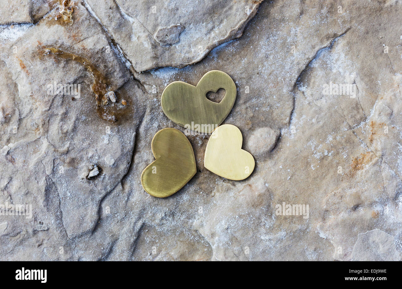 Tre luminose bellissime cuori di metallo sono collocati su una roccia con sale naturale su una spiaggia. Foto Stock