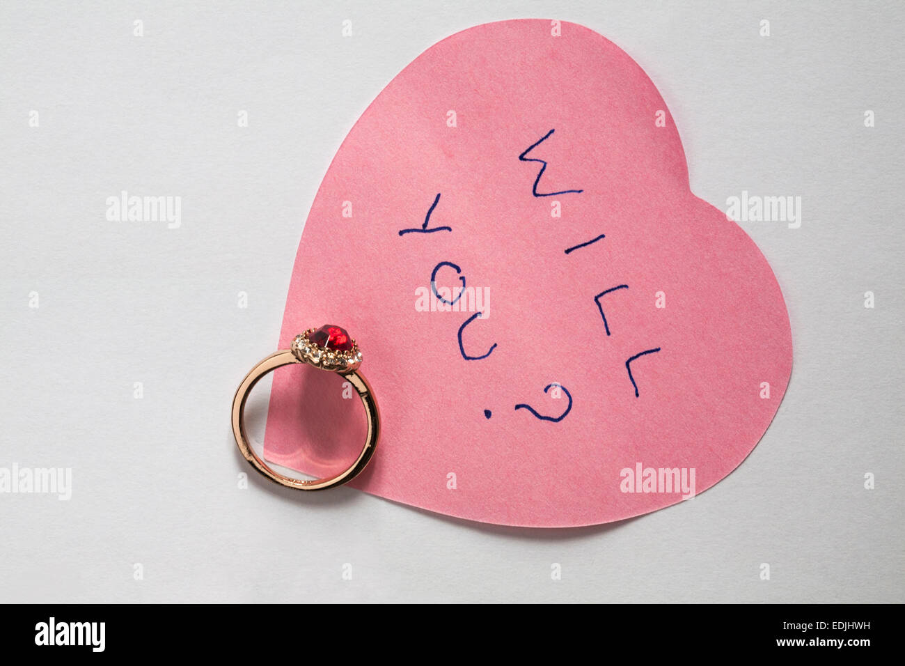 Sarà lei? Messaggio scritto sul rosa a forma di cuore post-it con anello di fidanzamento - proposta di matrimonio isolati su sfondo bianco Foto Stock