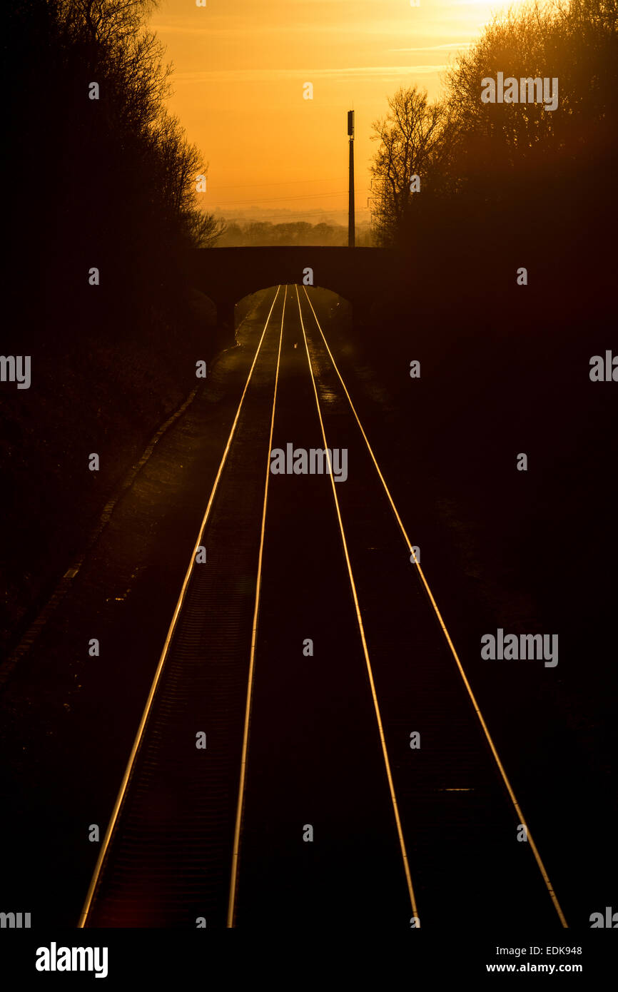 Un cielo arancione dipinge la discesa con stagliano binari del treno e il ponte come la serata in testa al tramonto Foto Stock