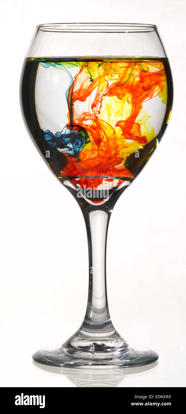 Bicchiere da vino con acqua e diversi coloranti alimentari Foto Stock