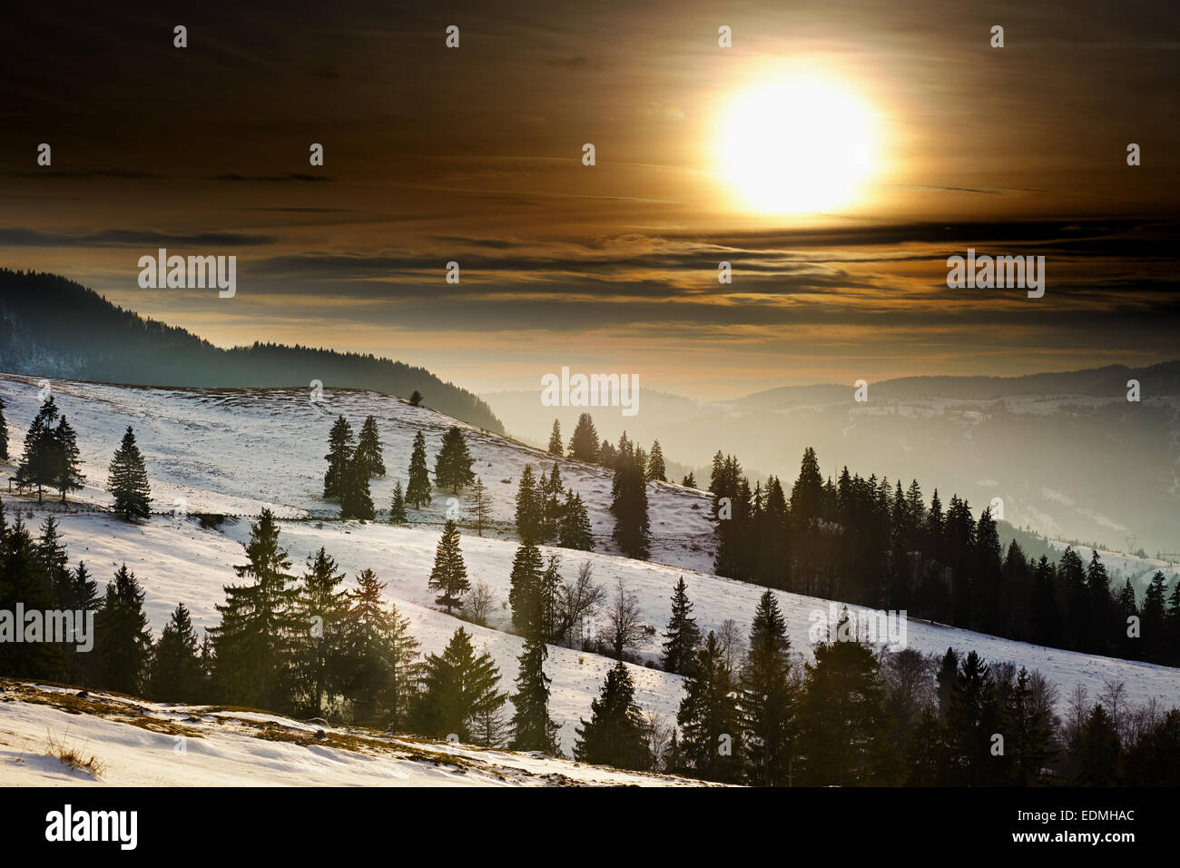 Paesaggio invernale con il sole che tramonta e le montagne con alberi di pino Foto Stock