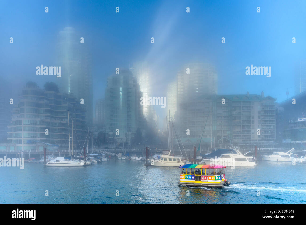 Yaletown highrises riflettere sunburst attraverso la nebbia mentre colorate traghetto passeggeri taxi attraverso acque di False Creek, Vancou Foto Stock