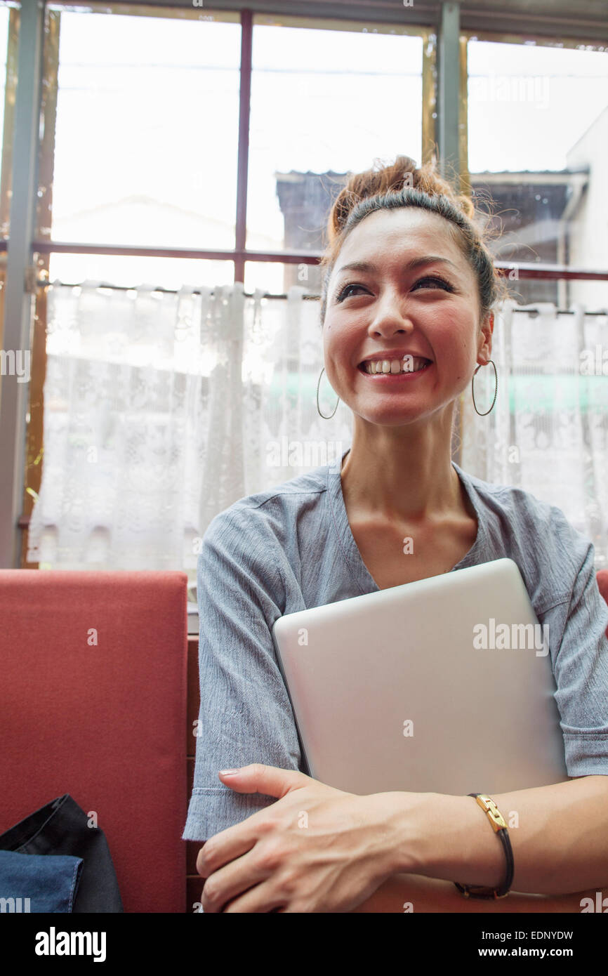 Donna che mantiene un notebook nelle sue braccia e di seduta all'interno. Foto Stock