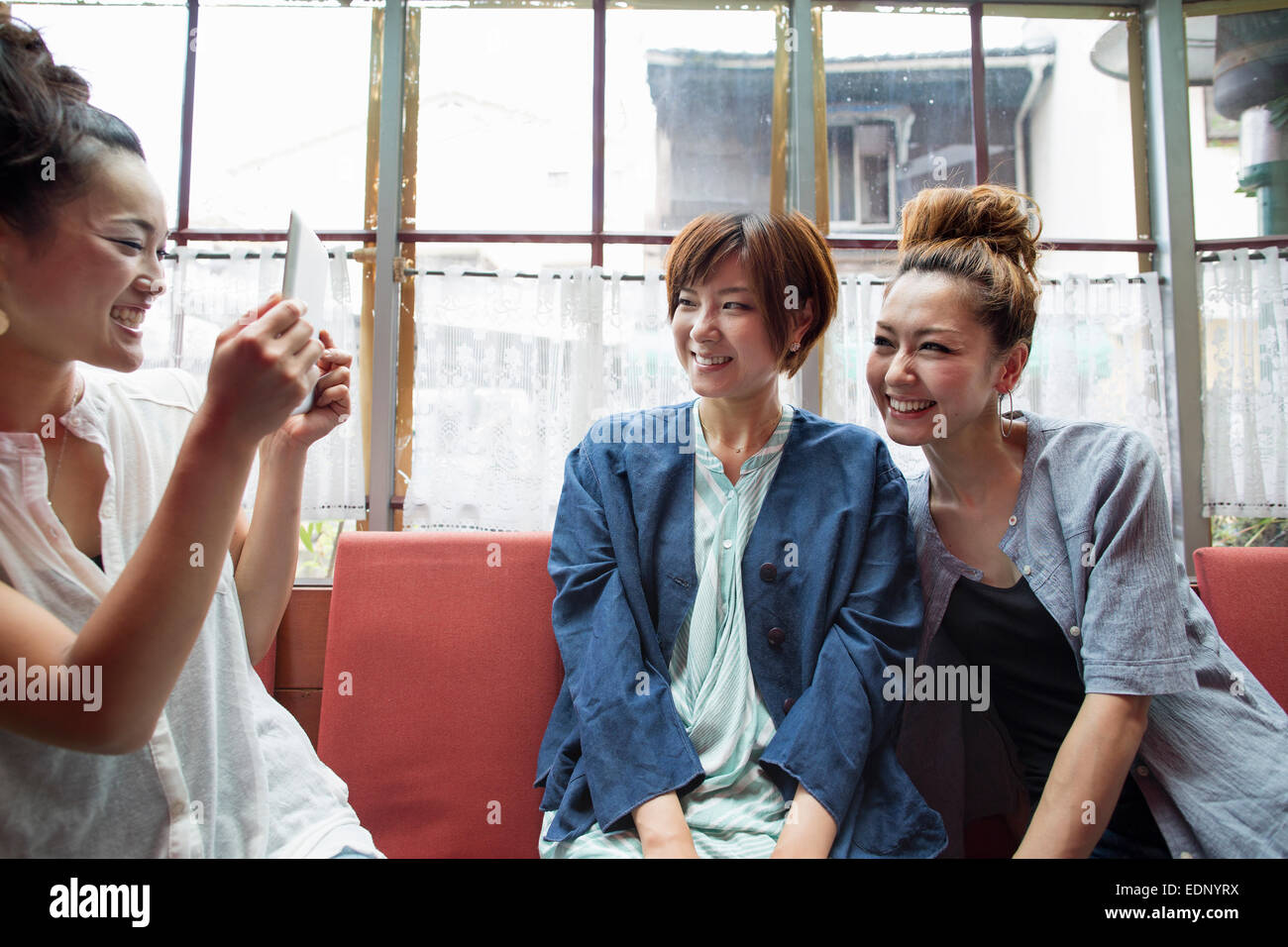 Tre donne sedute in interni, una holding una tavoletta digitale, tenendo l'immagine. Foto Stock
