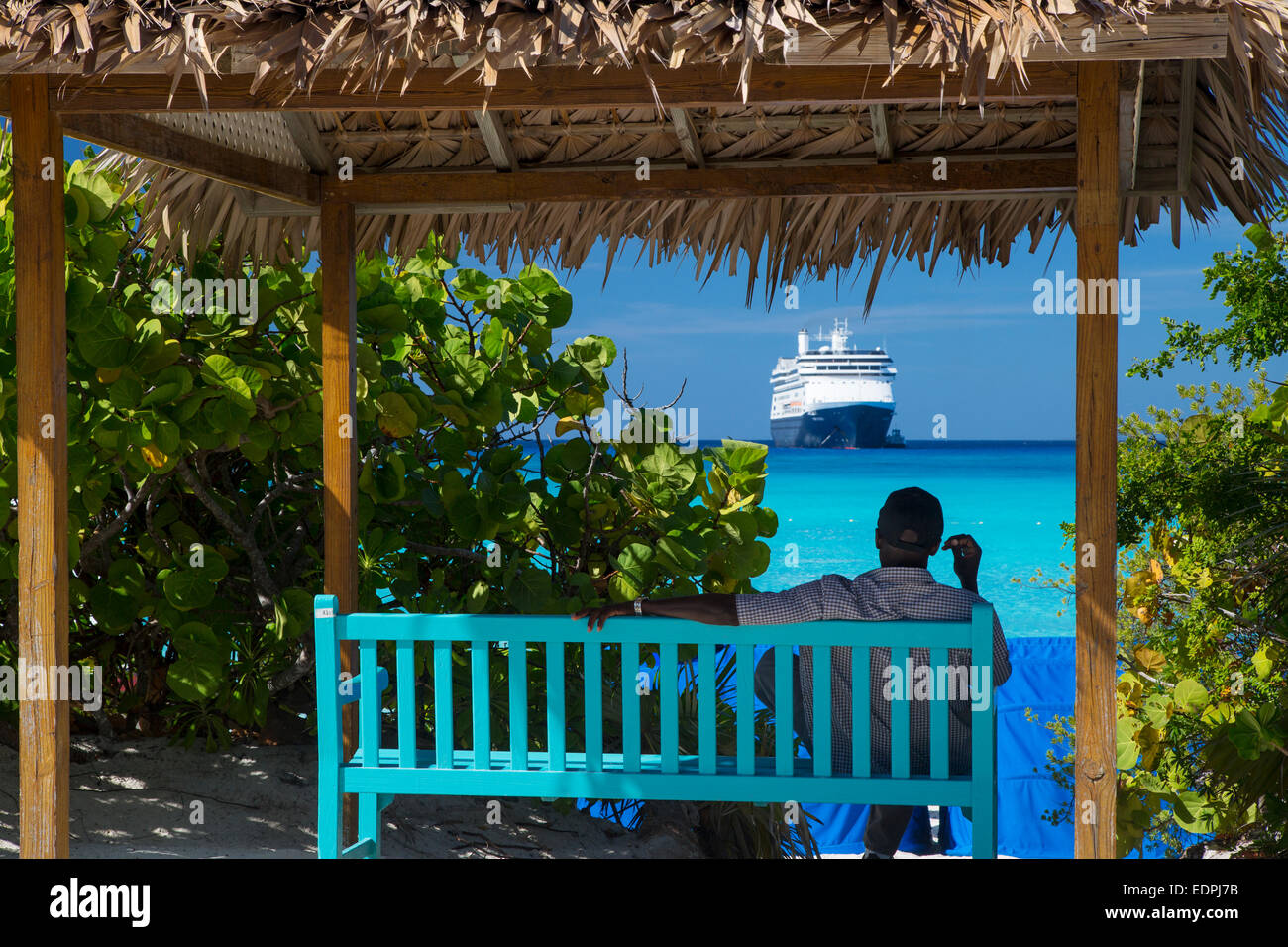 L'uomo rilassarsi all'ombra su Half Moon Cay con Holland America Cruise Line 'Amsterdam' ancorata al di là, Bahamas Foto Stock