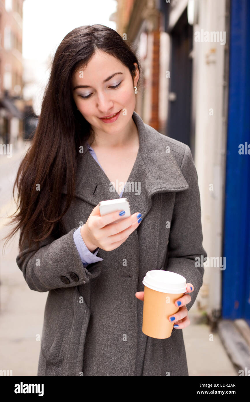 Giovane donna controllare i suoi messaggi di testo con un caffè Foto Stock