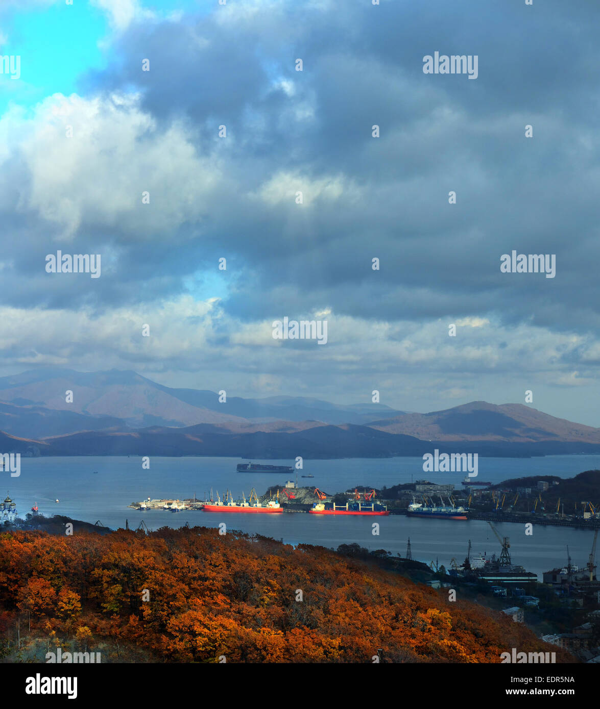 Navi sotto carico nel porto di Nakhodka sullo sfondo di nuvole e fogliame giallo Foto Stock