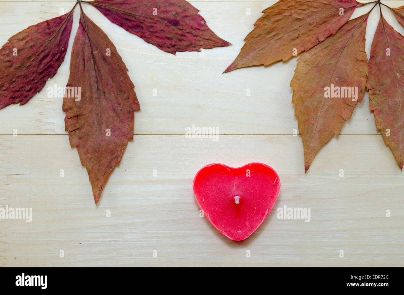 Asciutto e colorato Foglie di autunno e un rosso a forma di cuore ad candela su una tavola di legno Foto Stock