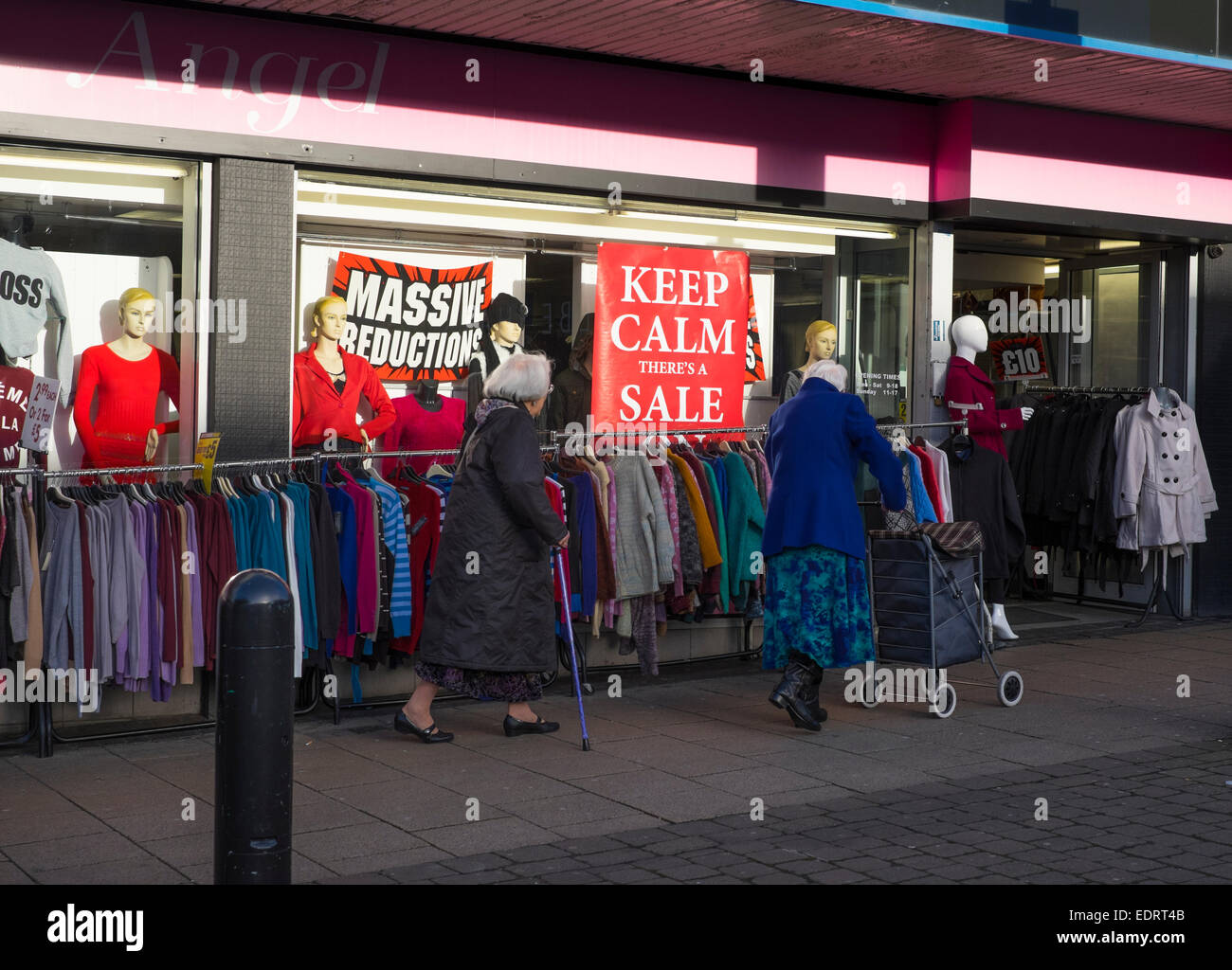 Due donne anziane a piedi passato un negozio di abbigliamento con vendita di segni, Walsall, West Midlands, Inghilterra. Foto Stock