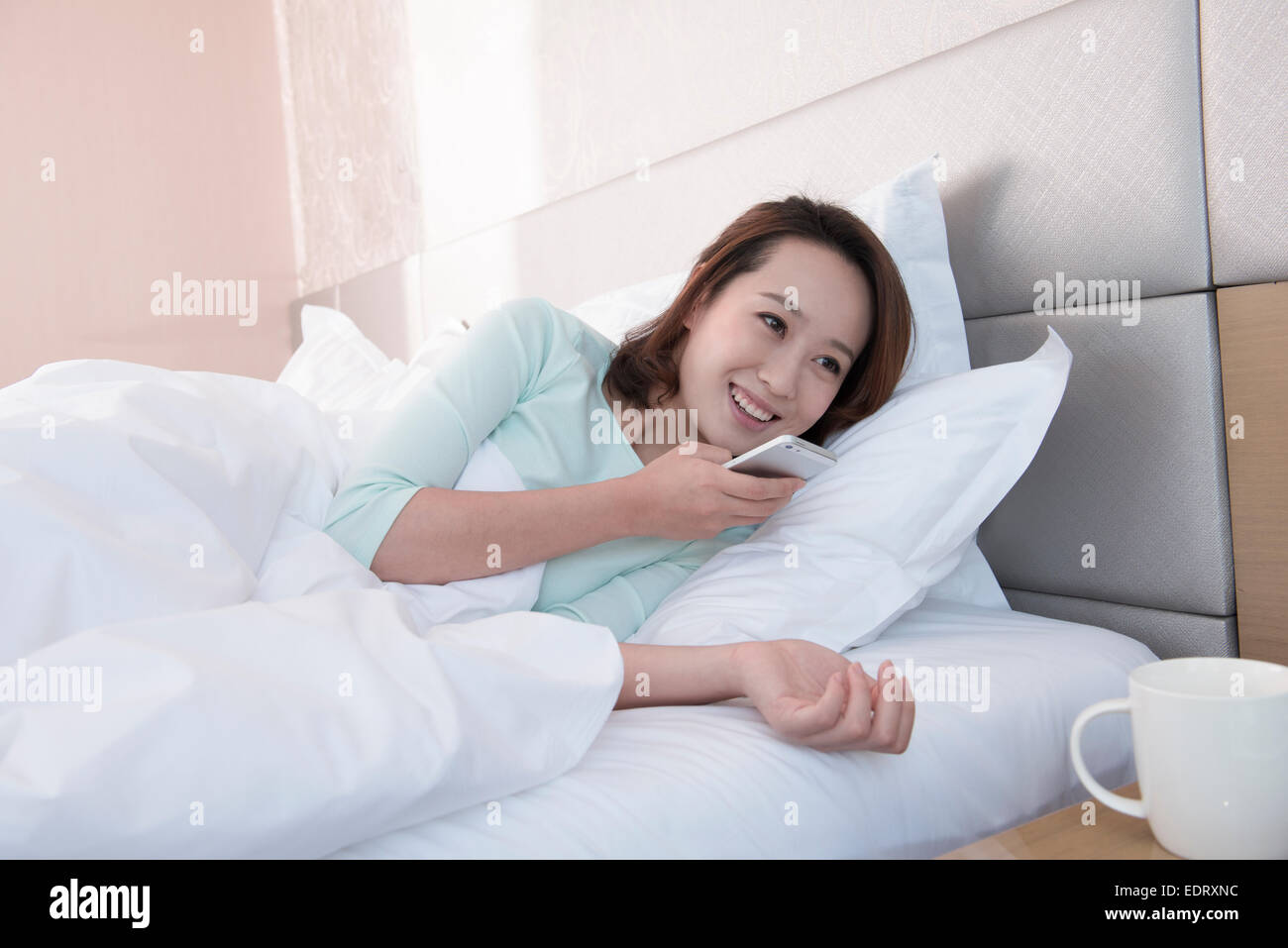 Giovane donna invio di messaggio vocale nel letto Foto Stock