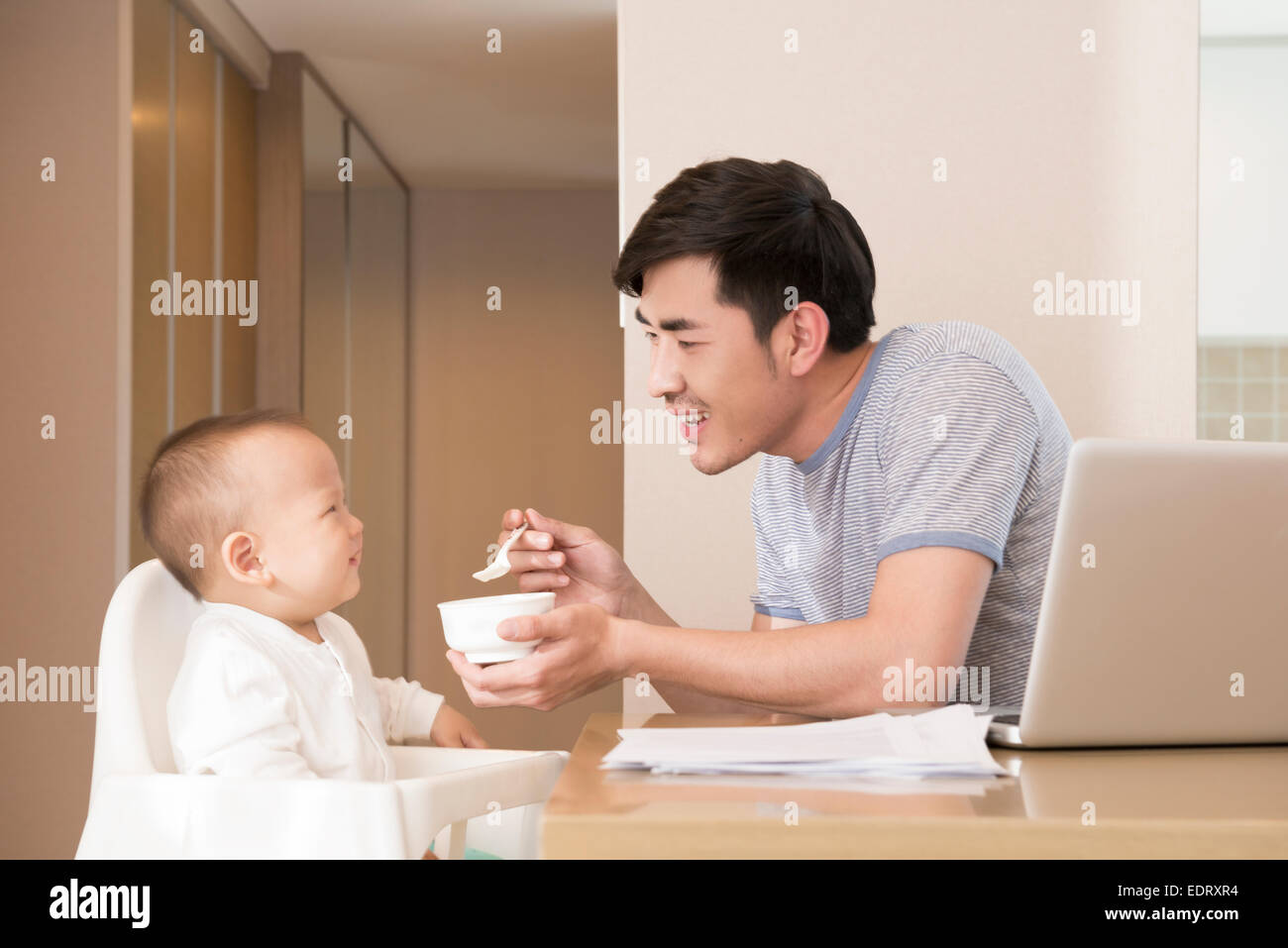 Giovane padre lavorare mentre si alimenta baby boy Foto Stock