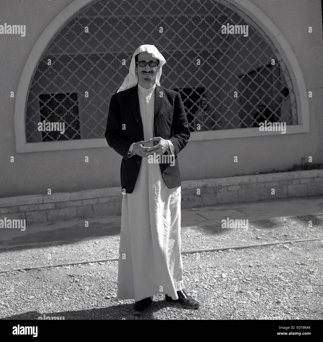 1950 storiche, la foto di un insegnante di arabo con headress e abiti lunghi in piedi fuori, Saudia Arabia. Foto Stock