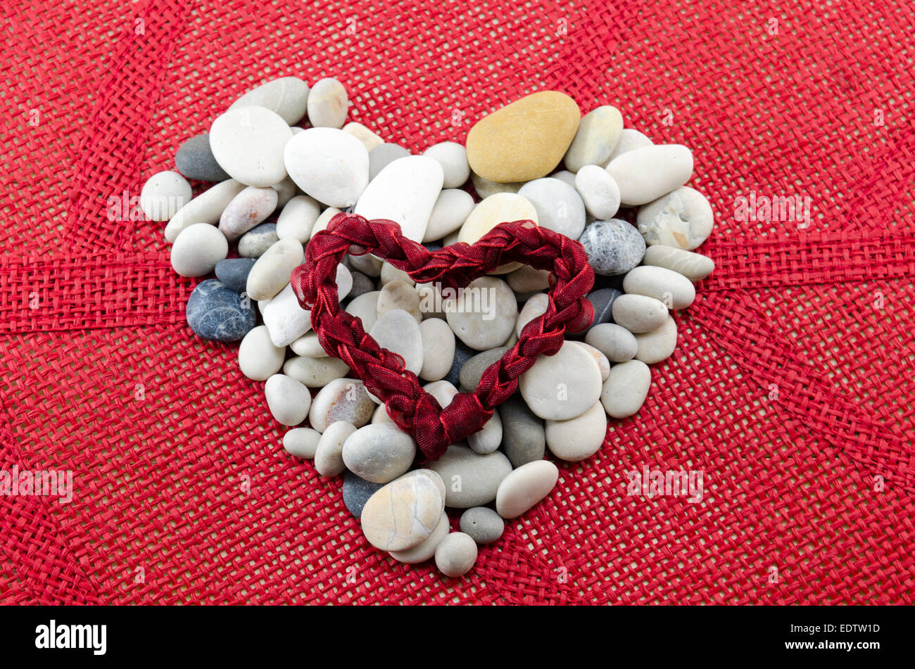 Ciottoli sagomata in un cuore con un cuore di pizzo su una superficie di colore rosso Foto Stock