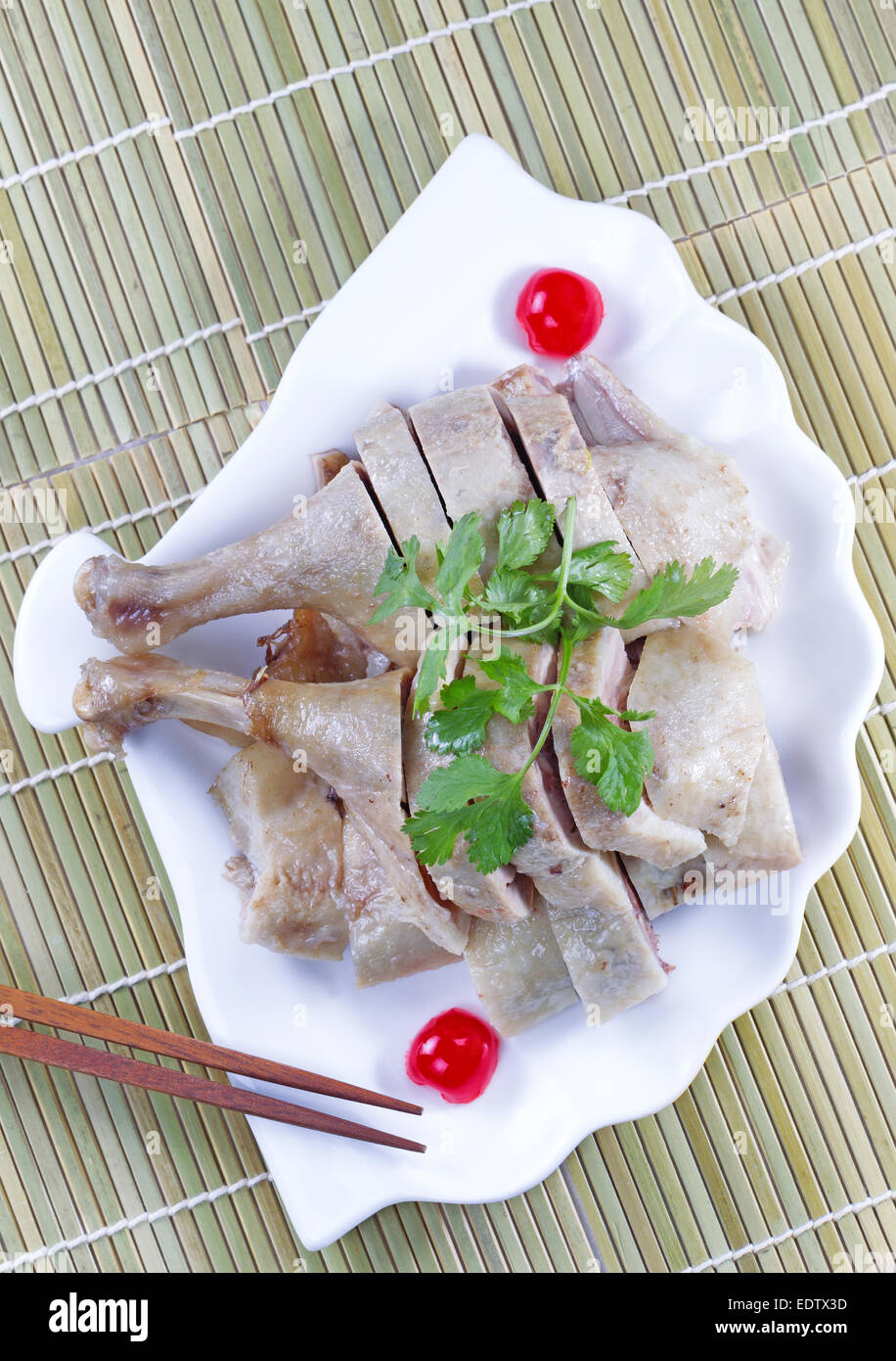 Verticale in alto visualizza immagine di cinesi il pollo cotto, prezzemolo, ciliegia e bacchette in guscio a forma di piastra bianca Foto Stock
